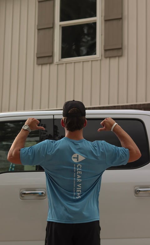 Person in blue t-shirt flexing muscles with arms raised, standing in front of silver van and building with window