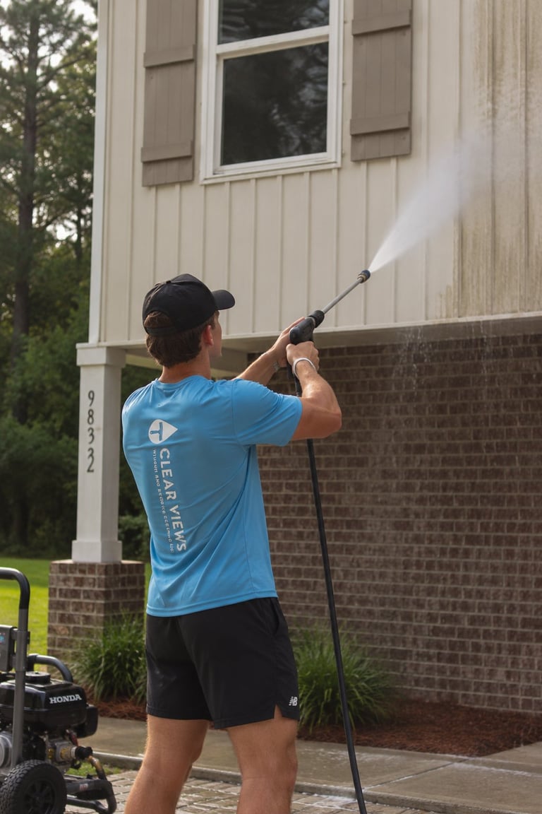 Man in blue shirt power washing brick exterior wall of house with pressure washer